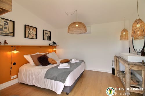 Chambre moderne aux Écuries du Bout du Monde, Landunvez, avec tête de lit orange, luminaires en osier et salle d'eau privée