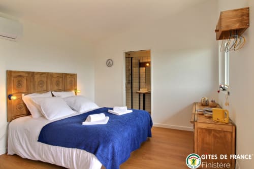 Chambre douillette au gîte Les écuries du bout du monde à Landunvez : lit en bois, couverture bleue, salle de bain privée et jardin