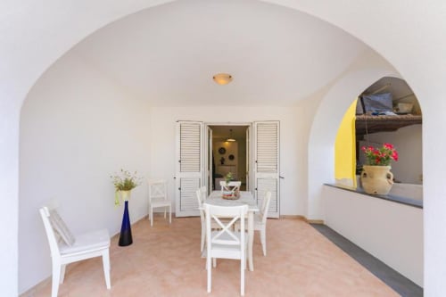 Luminosa zona pranzo con soffitto ad arco nella maisonette IL POETA, Procida. Fiori in vaso e vaso azzurro.