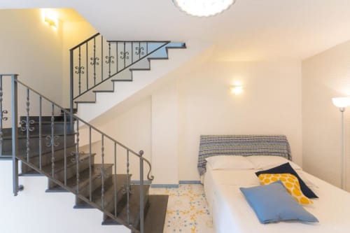 Camera da letto in maisonette a Procida con scala moderna, letto bianco con cuscini blu e ringhiere in ferro battuto