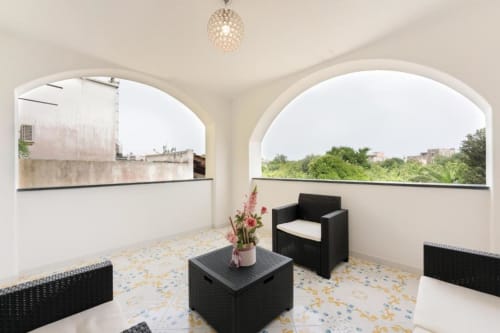 Terrazza luminosa con mobili in vimini nero, finestre ad arco e vista sul giardino della maisonette Il Poeta a Procida, Italia