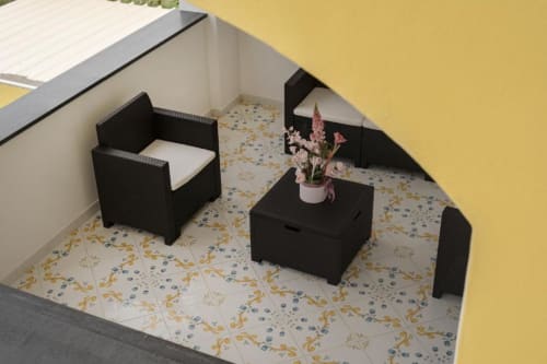 Zona living della maisonette moderna a IL POETA Procida con poltrona in vimini nero, tavolino e fiori rosa su motivi decorativi