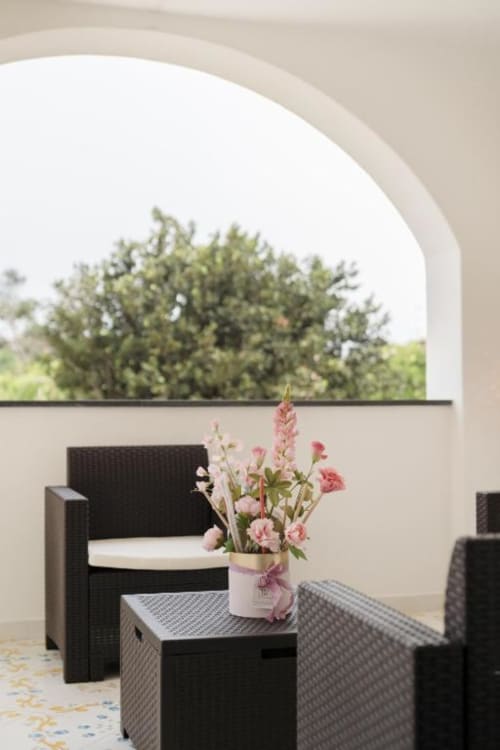 Terrazza maisonette di Procida con arredi neri, composizione floreale rosa e vista giardino sotto arco moderno