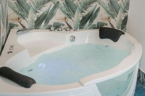 Vasca idromassaggio lussuosa riempita di acqua azzurra presso IL POETA, Procida. Sfondo con carta da parati a foglie tropicali