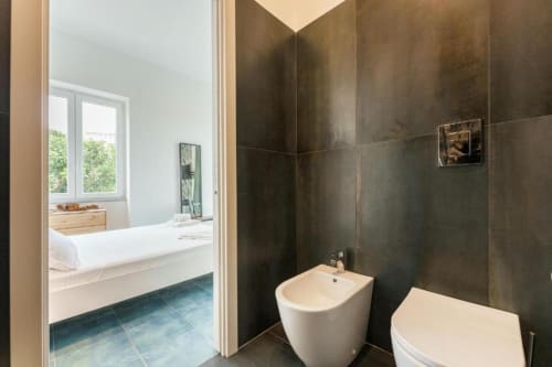 Bagno moderno in IL POETA Procida con pareti piastrellate scure, bidet e wc bianchi, vista oceano dalla porta aperta