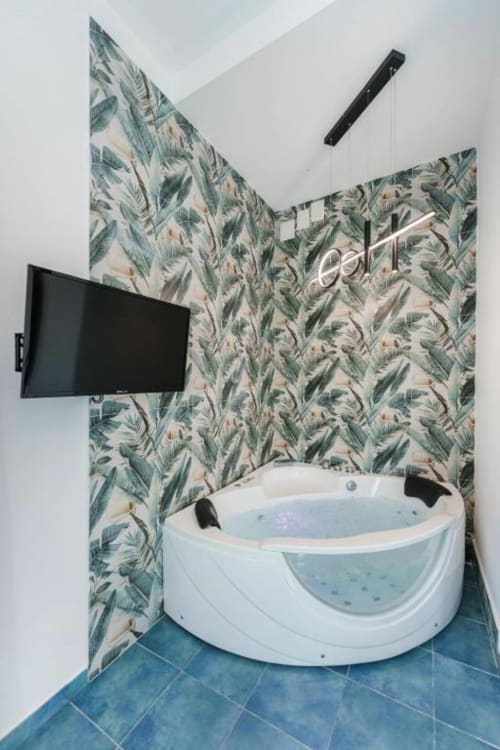 Moderna vasca idromassaggio con carta da parati a foglie tropicali e TV a muro all'hotel IL POETA di Procida, Italia