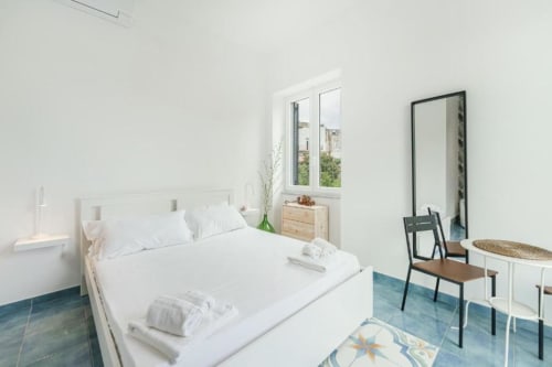 Camera da letto luminosa con vista mare presso Il Poeta B&B, Procida: biancheria bianca, cassettone in legno e pavimento con piastrelle blu