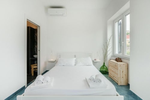 Camera da letto moderna con letto queen size, biancheria bianca, cassettone in legno, finestre con vista mare e arredamento minimalista presso IL POETA B&B a Procida