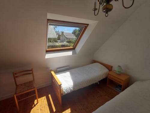 Chambre lumineuse du gîte Locmaria avec fenêtre de toit, lit en bois, fauteuil et vue sur le jardin de Belle Île en Mer