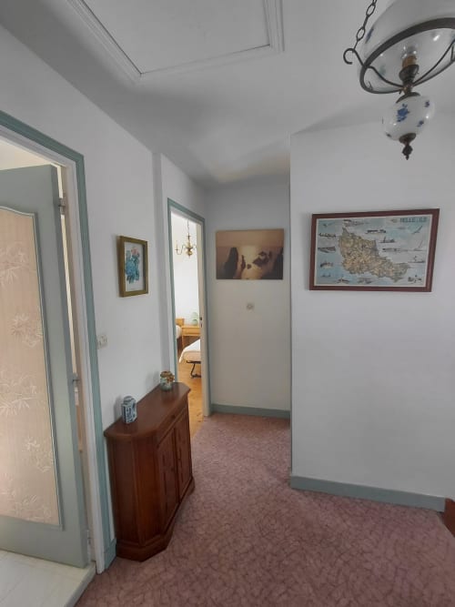 Couloir de la maison Lannivrec avec portes aux encadrements bleu-canard, commode en bois et tableau géographique sur murs blancs