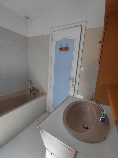 Salle de bains avec vasque ronde marron, baignoire, murs carrelés et porte bleue, cottage Maison Lannivrec, Belle Île en Mer, France