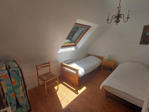 Chambre mansardée lumineuse avec deux lits, mobilier en bois, fenêtre de toit et lustre traditionnel à la Maison Lannivrec