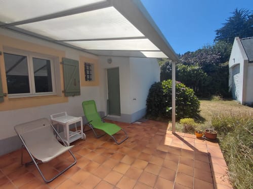Terrasse de cottage avec auvent, chaise longue verte, fauteuil blanc et vue sur le jardin à Locmaria, Belle Île en Mer
