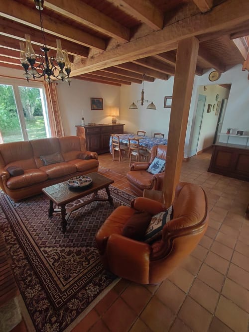 Spacieux salon de cottage avec sièges en cuir, poutres apparentes, cheminée et salle à manger avec vue sur le jardin à Locmaria