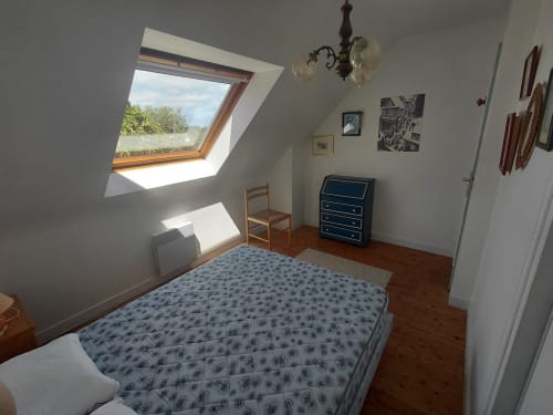 Chambre lumineuse sous les toits du gîte de Locmaria avec lucarne, parquet, lit aux motifs bleus, bureau et vue sur le jardin