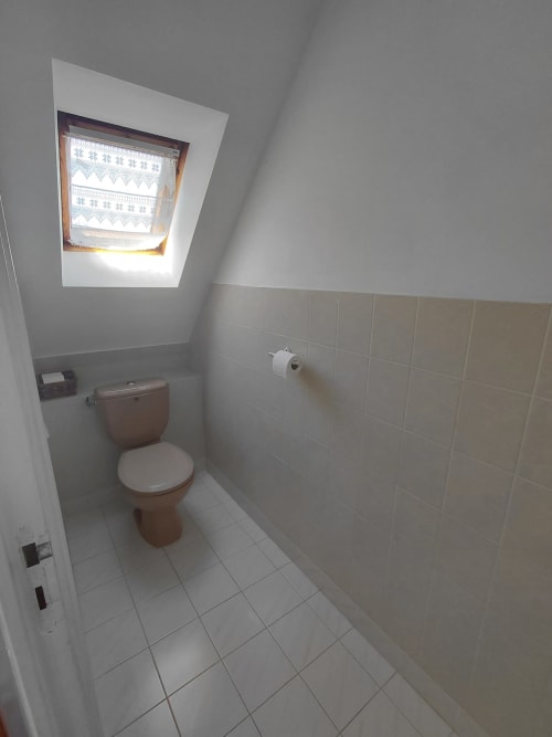 Salle de bains mansardée avec toilettes, lucarne et carrelage beige dans la location Locmaria