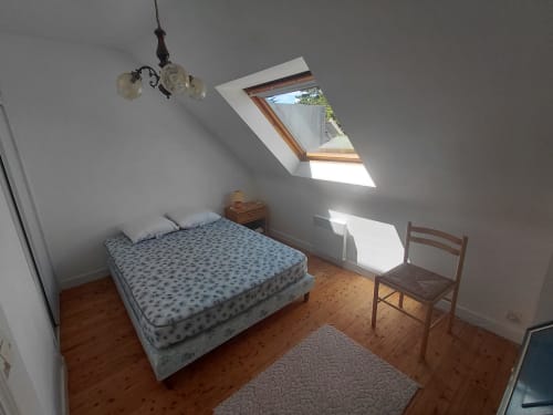 Chambre lumineuse sous les combles du gîte Locmaria avec puits de lumière, parquet, lit, fauteuil et suspension