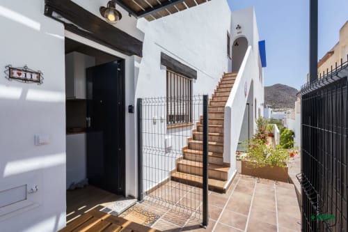 Entrada del apartamento Manbea 11 en Almería con muros blancos, puerta negra, escaleras de madera y vistas a las montañas desérticas
