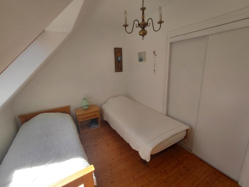 Chambre mansardée douillette avec deux lits simples, table de nuit en bois, lustre en laiton et armoire au gîte Maison Lannivrec