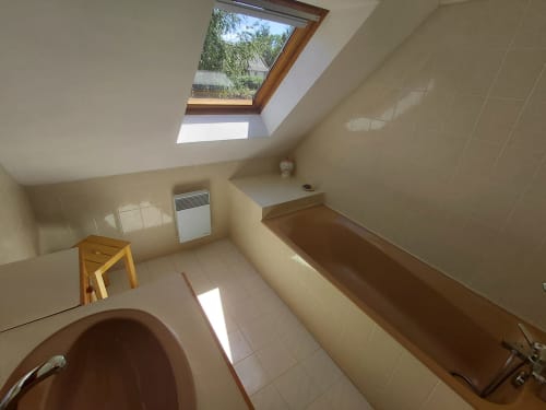 Salle de bains mansardée du gîte Maison Lannivrec à Locmaria Belle-Île avec lucarne, baignoire marron et carrelage