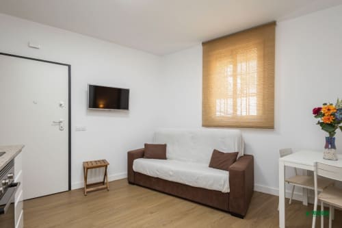 Manbea 11 apartment in Almería: Modern living room with brown sofa, white walls, wooden flooring, and natural light from