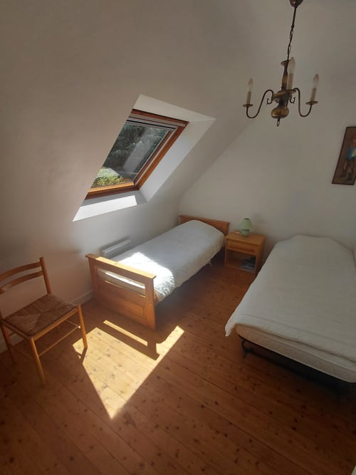 Chambre lumineuse sous les toits du gîte Locmaria avec lits en bois, lucarne et mobilier rustique