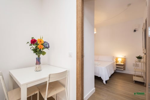 Manbea 11 room in Almería with white table, colorful flowers, and bedroom view with white bedding