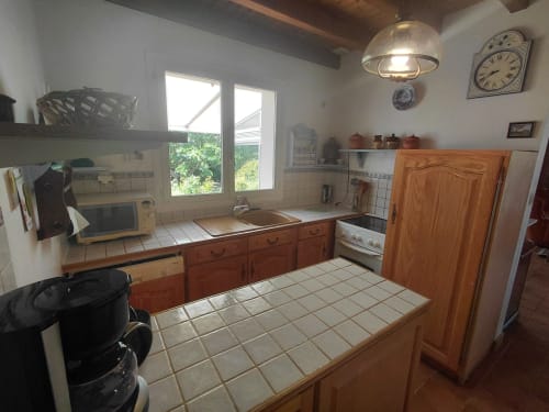 Cuisine de cottage à Locmaria avec meubles en bois, comptoirs carrelés, cuisinière, évier et vue sur le jardin