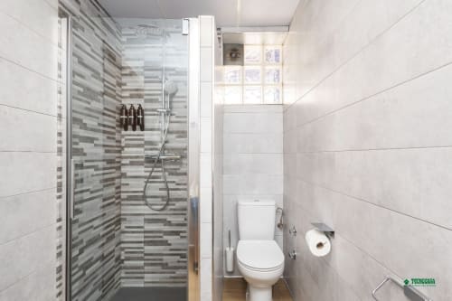 Modern bathroom at Apartamentos Manbea in Almería with glass shower, striped tile accent wall, and white toilet