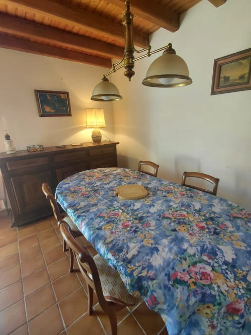 Salle à manger du cottage Maison Lannivrec avec nappe à fleurs bleues, poutres en bois, luminaires suspendus en laiton et style rustique français