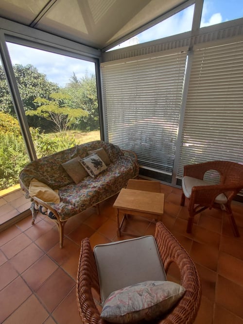 Véranda ensoleillée avec canapé à motifs, fauteuils en rotin et vue sur le jardin à la Maison Lannivrec, Belle Île en Mer