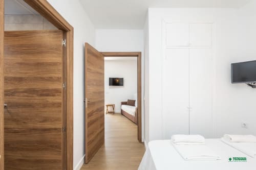 Modern hotel room at Apartamentos Manbea in Almería with wooden doors, white bedding, and view into connecting bedroom suite