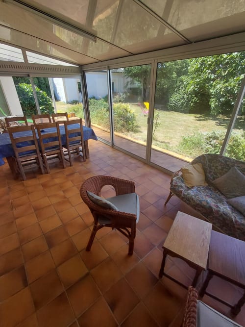 Véranda ensoleillée aux carreaux en terre cuite, table à manger, fauteuil en rotin et vue sur le jardin du gîte Maison Lannivrec, Belle Île en