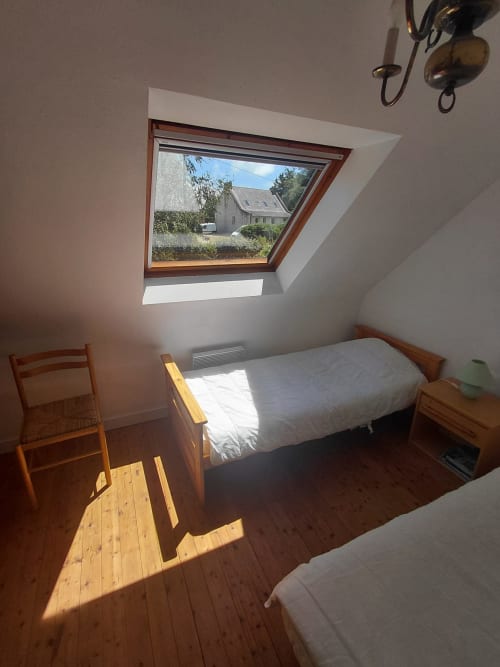 Chambre lumineuse sous les toits avec lit en bois, lucarne donnant sur le jardin et plancher ensoleillé à Maison Lannivrec