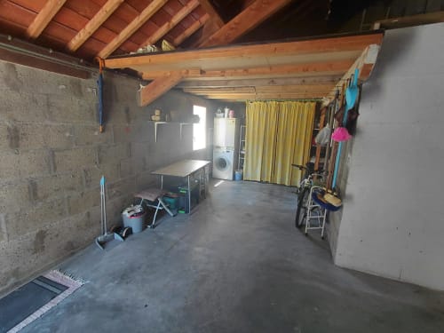 Intérieur spacieux de garage-studio avec poutres en bois, sol béton, machine à laver, rideaux jaunes et rangements