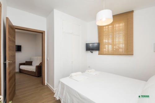 Modern bedroom at Apartamentos Manbea in Almería with double bed, wooden doors, and flat-screen TV