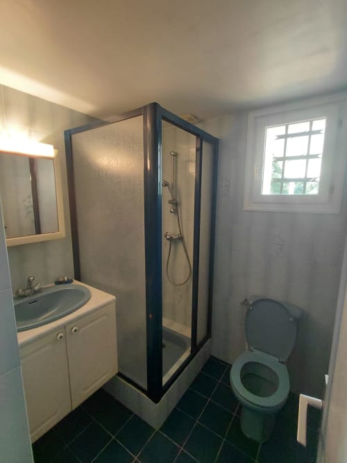 Salle de bain moderne du gîte Locmaria avec douche à cadre noir, lavabo, toilettes et fenêtre