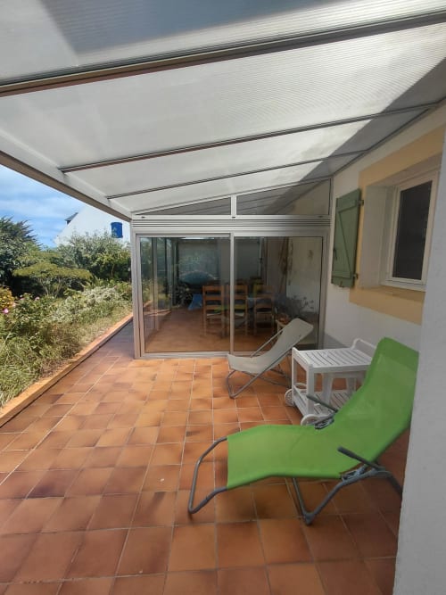 Terrasse couverte avec chaises vertes, table blanche et baies vitrées de la maison Lannivrec à Locmaria, Belle-Île-en-Mer