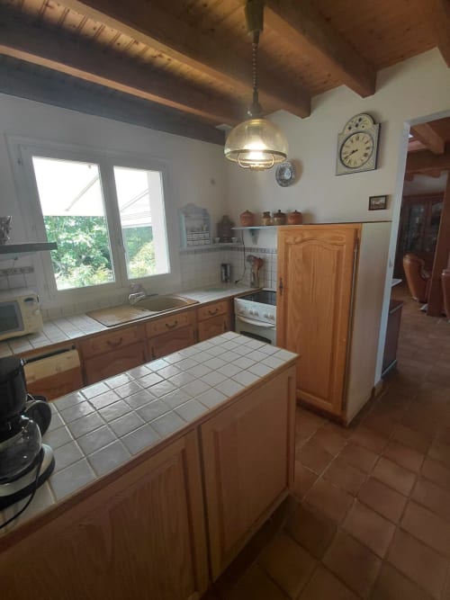 Cuisine de chaumière à Locmaria, Belle Île en Mer avec meubles en bois, plan de travail en carrelage blanc et vue sur le jardin