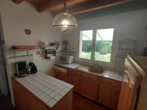 Cuisine spacieuse à Locmaria avec meubles en bois, plans de travail carrelés, baies vitrées sur jardin et appareils modernes