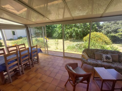 Véranda ensoleillée avec chaises de salle à manger, mobilier en rotin et vue sur le jardin du gîte Maison Lannivrec, Belle Île en Mer