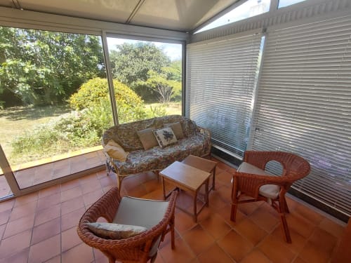 Véranda lumineuse avec fauteuils en rotin, canapé et vue sur le jardin du gîte Maison Lannivrec, Belle Île en Mer