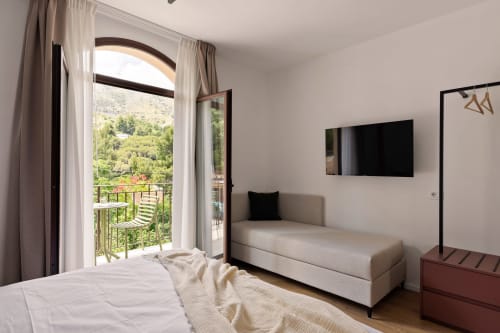 Luminosa camera d'albergo a Dimora Silva con letto, zona salotto, balcone con vista sulla verdeggiante collina di San Martino delle
