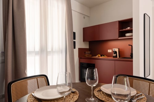 Zona pranzo nell'appartamento Dimora Silva con sedie in rattan, tavola apparecchiata e cucina moderna color ruggine sullo sfondo