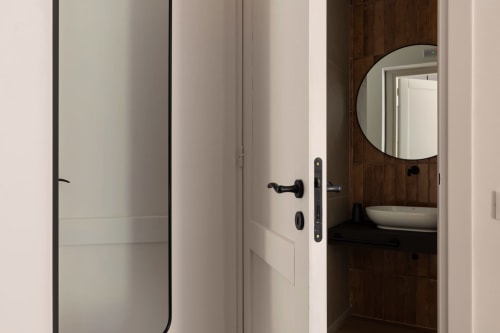 Ingresso moderno di Dimora Silva con maniglie nere, porte bianche e specchio rotondo che riflette il bagno