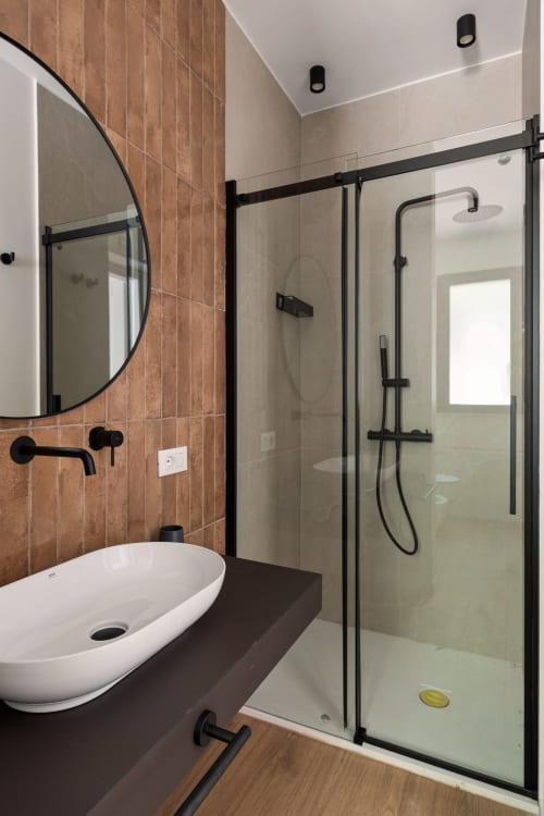 Bagno moderno presso Dimora Silva Nature Suites con piastrelle in terracotta, doccia con cornice nera, specchio circolare e lavabo bianco