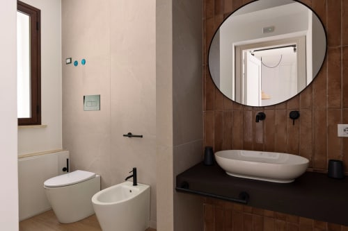 Bagno moderno nell'appartamento Dimora Silva 2 con sanitari bianchi, specchio rotondo e dettagli in piastrelle marroni presso Dimora Silva Nature