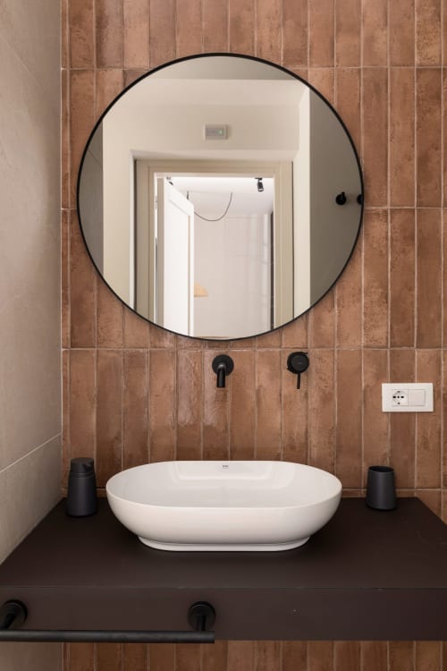 Bagno moderno presso Dimora Silva Nature Suites con specchio rotondo, lavabo bianco a bacile e pareti in cotto