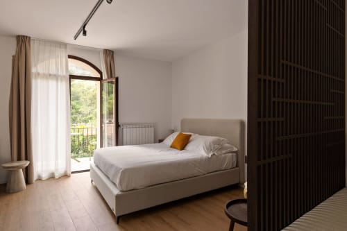 Camera da letto spaziosa di Dimora Silva Nature Suites con letto beige, porte ad arco che si aprono sul balcone, pavimenti in legno e luce naturale