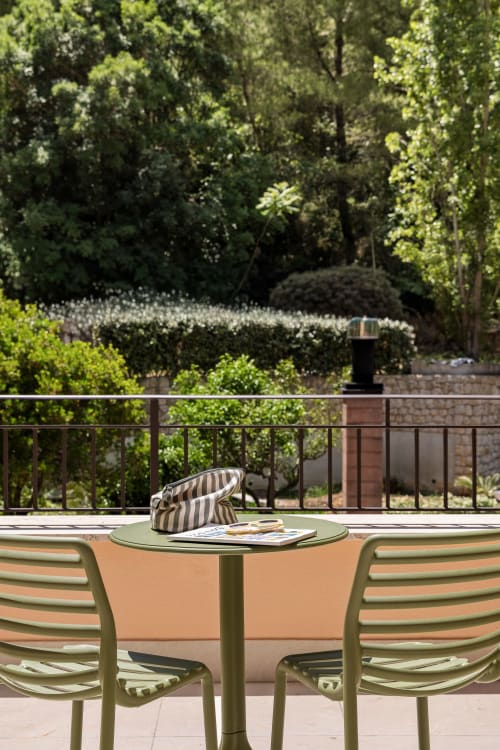 Outdoor patio at Dimora Silva Nature Suites with green chairs, small table, striped hat and magazine overlooking lush forest